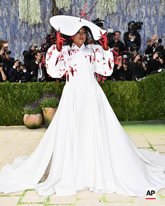 Naomi Osaka poses in a white gown and hat on the Met Gala carpet. 