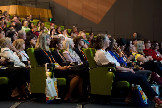 A large audience is seated in a modern auditorium, attentively watching a presentation at Women Deliver 2026.
