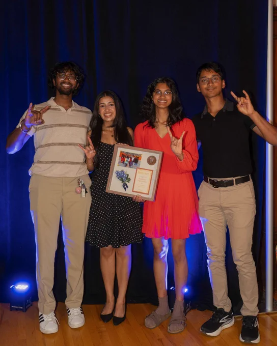 Slide 1: 4 students stand together holding a plaque with their hands in a "Hook 'Em Horns" position. 