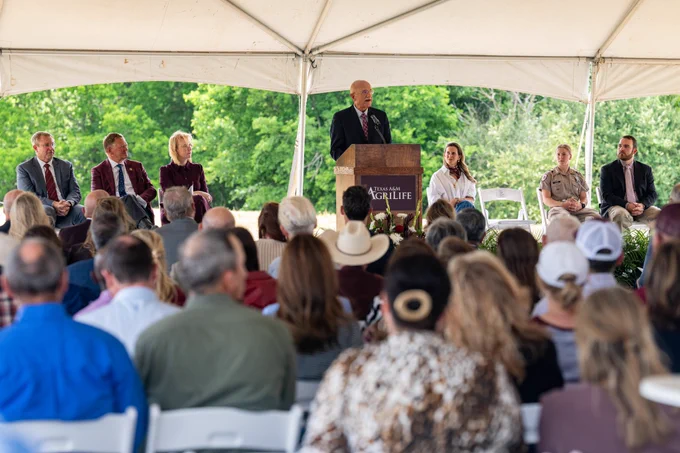 A group of individuals seated under a large canopy, with one person standing at a podium labeled "Texas A&M AgriLife".