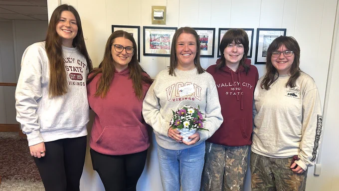 Erin Edinger standing between 4 students, holding flowers