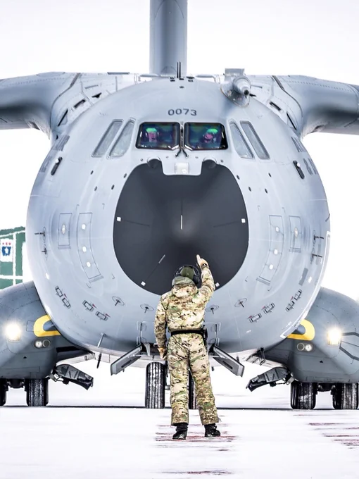A crew member directs a military aircraft on a snowy runway during an Arctic supply mission. Photo by Danish Armed Forces. Photo by Danish Armed Forces.