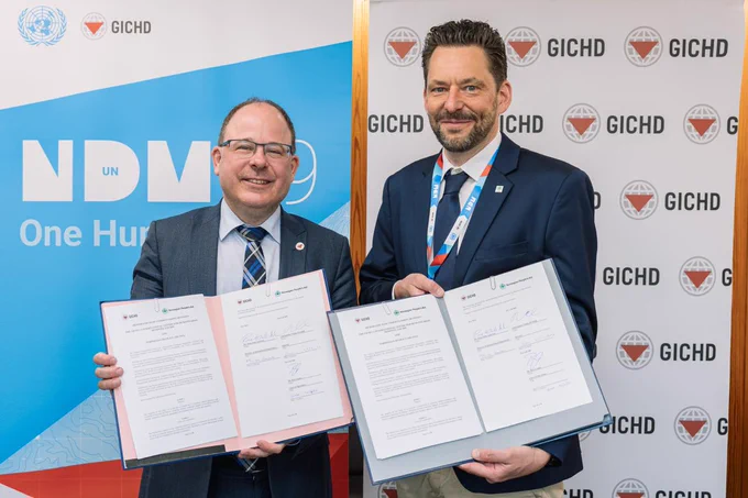 Smiling, GICHD Director, Ambassador Tobias Privitelli and Rune Kristian Dale-Andresen, Director of NPA's International Department, stand side by side holding signed MoU documents during the NDMUN29 event in April.