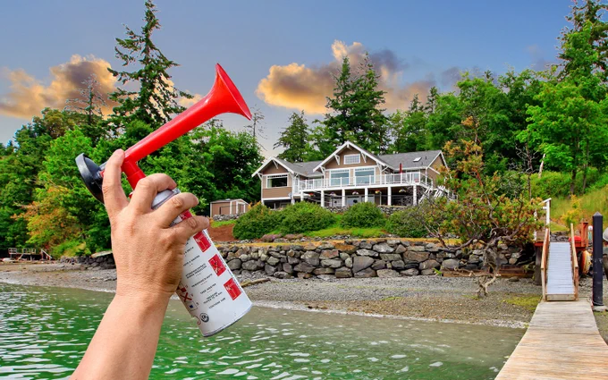 Man's hand holding airhorn outside waterfront home with dock