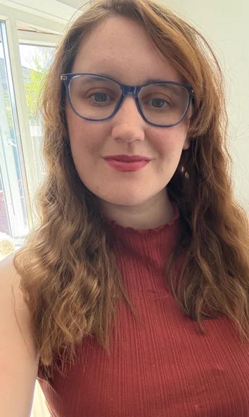 Picture of Sophie who has long brown hair and wears glasses. Has red top.