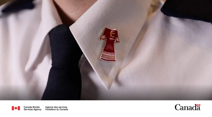 Close-up of a white uniform collar with a black tie and a red pin shaped like a traditional dress attached to the collar.