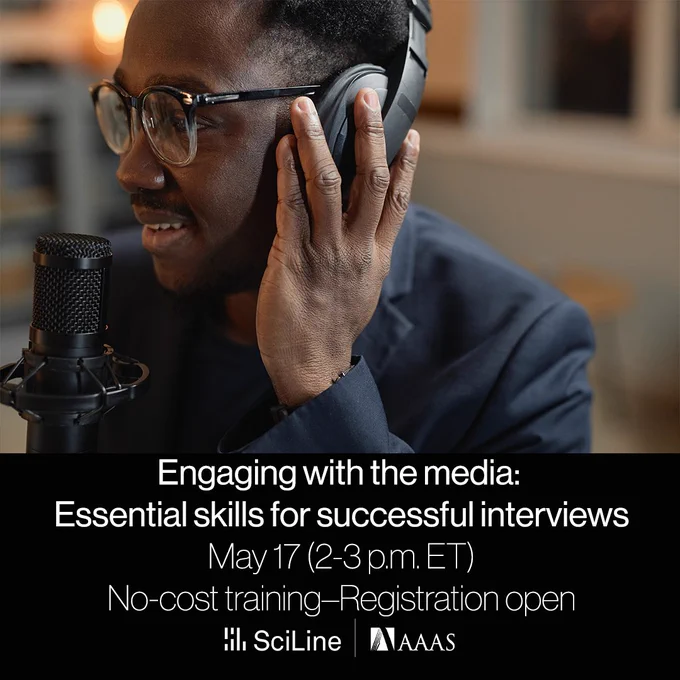 A person wearing glasses holds a set of headphones to his head while speaking into a microphone