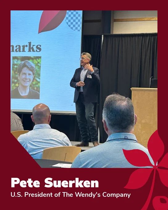 A person in a suit stands on a stage giving a presentation with a large screen displaying an image of another individual and the word "Remarks." The background includes a black curtain and a podium. The border of the image reads: "Pete Suerken, U.S. President of The Wendy's Company.