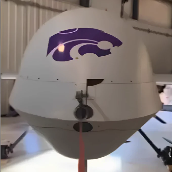 Close-up of a MQ-1 Predator unmanned aircraft system with a purple Kansas State University Salina Aerospace and Technology Campus wildcat mascot logo on its front nose section inside a hangar.