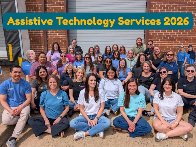 A large group of people are seated on a ramp outside a building a smiling for a group photo.