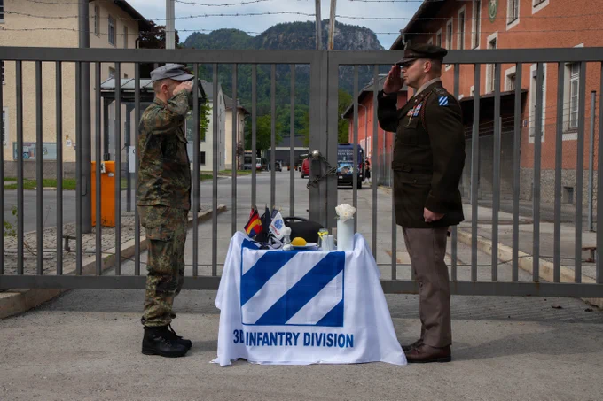 U.S. and German Soldier salute across a memorial table honoring the 3rd Infantry Division during a Bad Reichenhall  liberation anniversary ceremony.