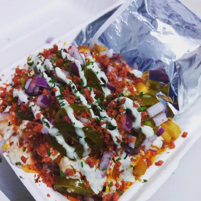A plate full of loaded french fries inside a plastic to-go container. 