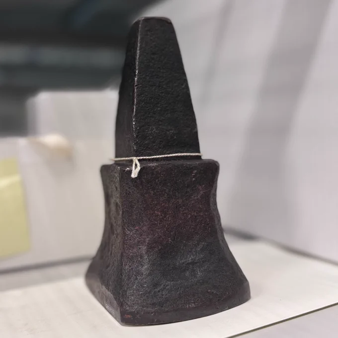 Une enclume de forge noire, au sommet effilé et à la base large, posée sur une surface blanche à l'intérieur.