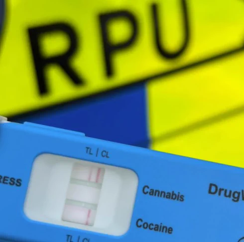 A blue drug test kit shows positive results for Cannabis and Cocaine, with an RPU uniform in the background.