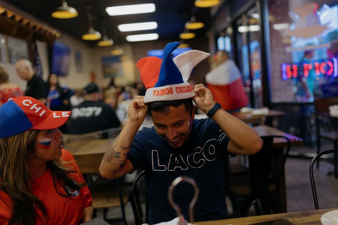 Two people wearing Chile-themed hats inside a lively restaurant with wooden tables and hanging lights.