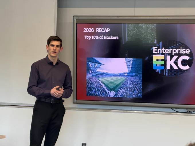 A man standing in front of a large display screen showing performance data for "Enterprise KC" event.