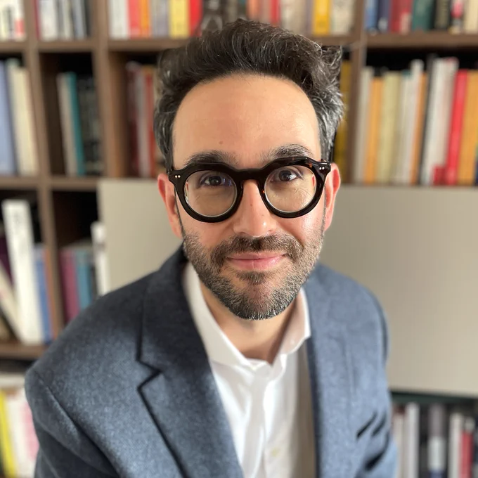 Assistant Professor Nicola Carboni smiles in front of shelves of books.