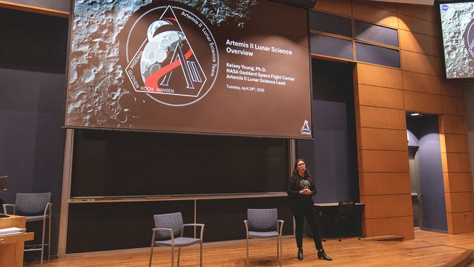 Kelsey Young stands on stage in a lecture hall beneath a large screen displaying “Artemis II Lunar Science Overview” during an Edison Lecture at Notre Dame.