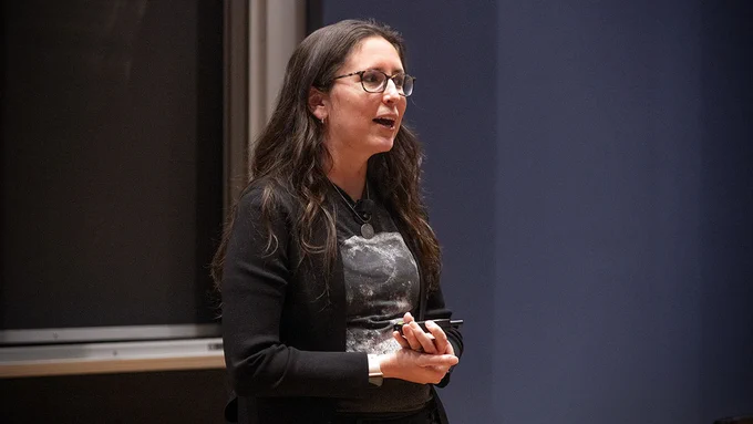Close-up of Kelsey Young speaking during her lecture, holding a presentation remote.