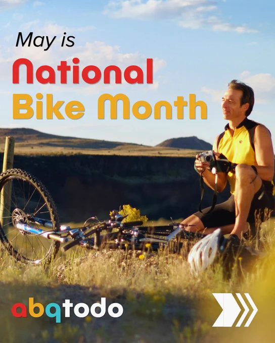 Cyclist resting on grass with bike and helmet, celebrating National Bike Month in May against a scenic landscape.
