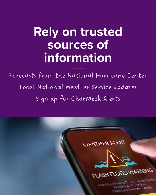 A smartphone displaying a weather alert for a flash flood warning. The screen shows a triangle with an exclamation mark. Above the phone, white text on a purple background reads: "Rely on trusted sources of information. Forecasts from the National Hurricane Center, local National Weather Service updates, sign up for CharMeck Alerts.