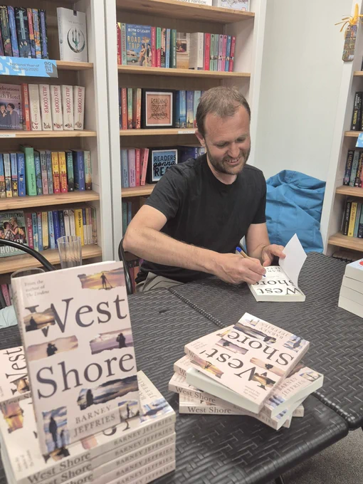 Man signing books called West Shore, against a backdrop of books