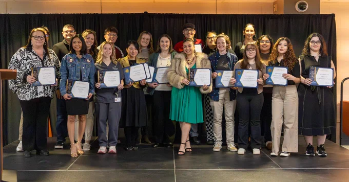 A group of individuals stand on a stage holding certificates.