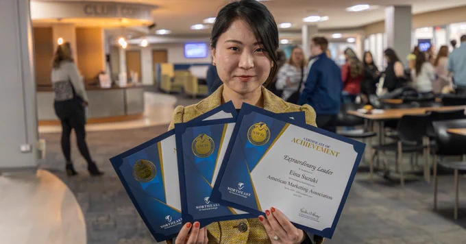 A person standing indoors holds three award certificates. 