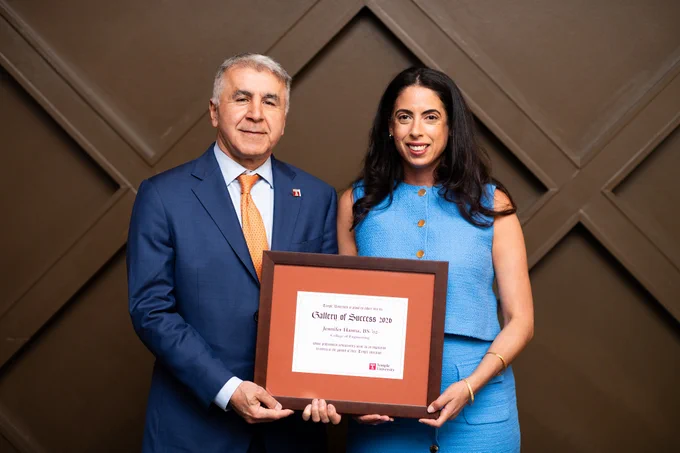 A man in a suit and tie stands next to a woman in a business professional outfit. They are both holding the same frame with a certificate celebrating the woman as  2026 Gallery of Success honoree.