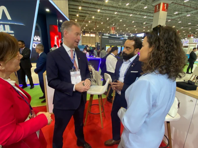 A man in a suit standing and talking to two women and a man on the floor of a trade exhibition 