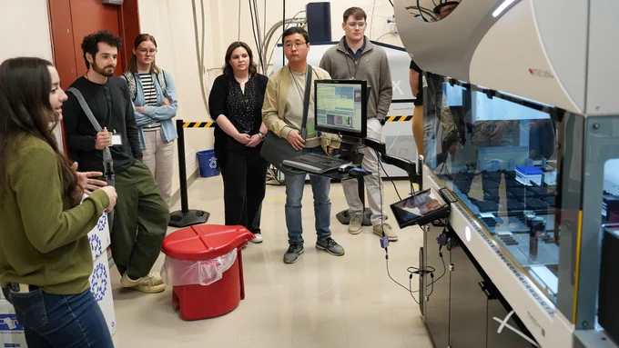 Photo of EMSL researcher standing next to laboratory equipment, presenting to event attendees.