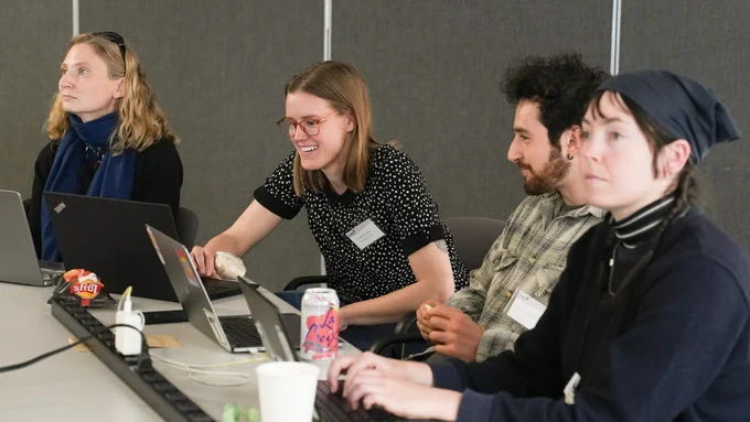 Photo of four event attendees watching a presentation or looking at laptops.