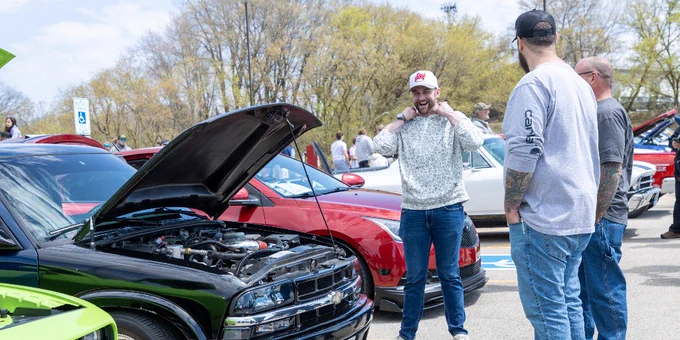 A group of people looking at a black car with its hood open at a car show.