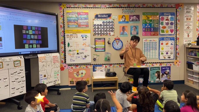 Henry Ngo in a classroom with students teaching them numbers and the ABCs