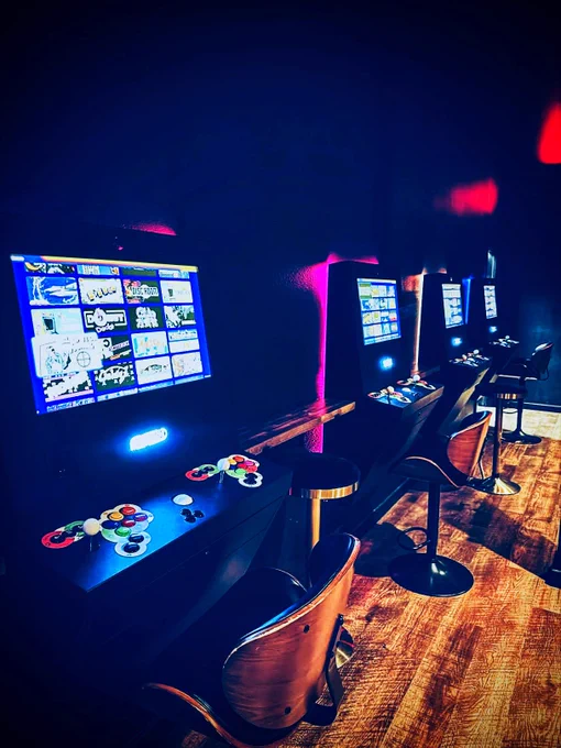 Row of Polycade arcade game machines with colorful buttons and bright screens in a dimly lit room with wooden flooring.