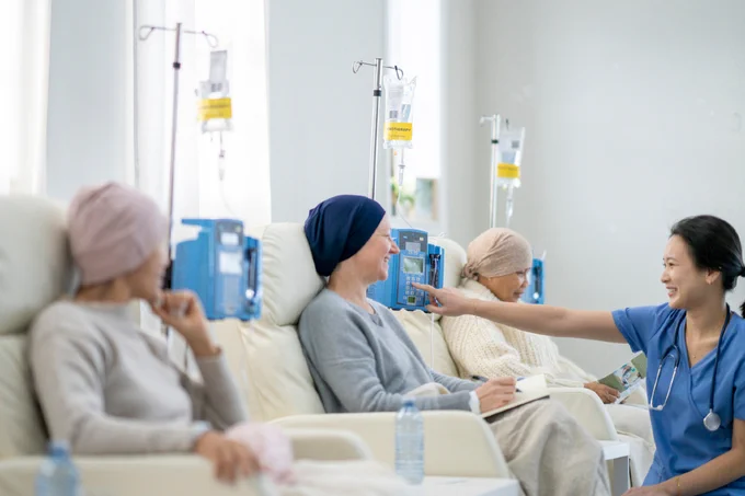 Tres personas con pañuelos, sentadas en sillones con bombas de infusión; una enfermera sonriente ajusta el equipo.