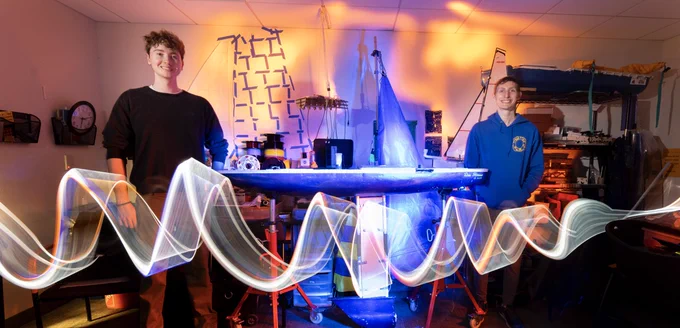 Leo Goldberg and Aaron Gan in the SailBot office with the sailbot in center of the photo