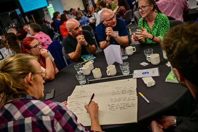 group of people sitting around a table having a discussion at the ASDC Conference, one person is writing down notes on a flip chart pad