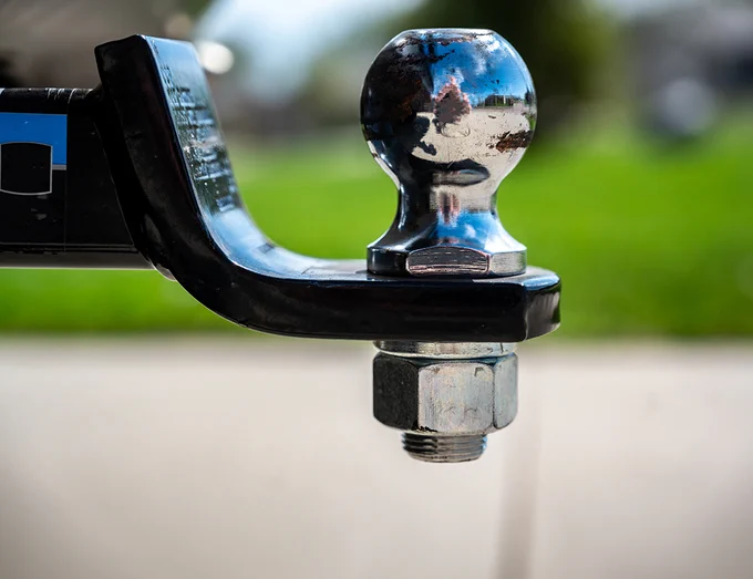 A shiny, chrome trailer hitch ball attached to a tow bar, with a grassy field and blurred background.