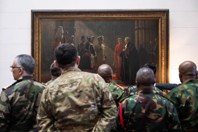 Group of military personnel in various uniforms observing a large historical painting inside a gallery or museum.