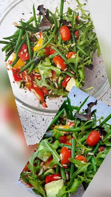 In a glass bowl is a beautiful salad of green leaves and herbs, red tomatoes, yellow peppers, green cucumber and beans, rice and seeds