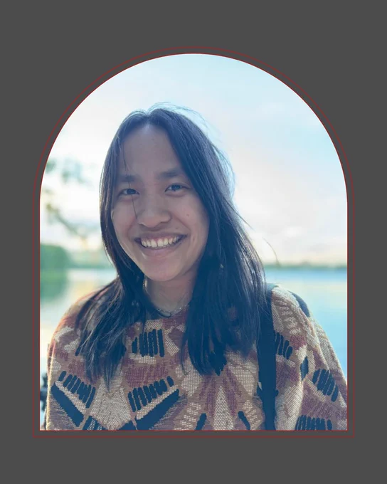 Within the shape of an arch, a picture of an Asian American woman with long black hair, smiling widely. She's wearing a multicolored shirt and standing outside near water, but her face is in shadow.