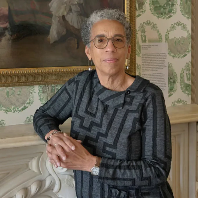 Jane Rhodes standing in front of a framed painting and ornate wallpaper.