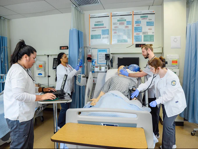 A diverse group of nurses work on a mannequin patient in a simulation lab at Cecil College