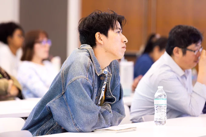 A man sits in a large lecture hall and listens to a man give a talk about his scientific research.