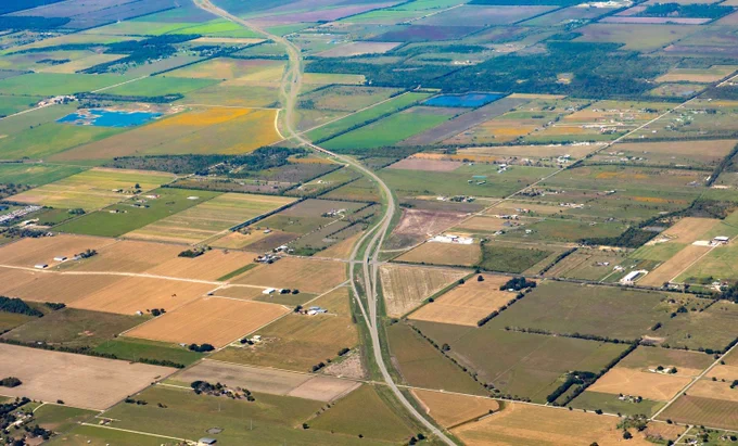 Aerial view of a rural landscape near Houston Texas with a winding road cutting through patchwork farmland fields in various shades of green and brown.