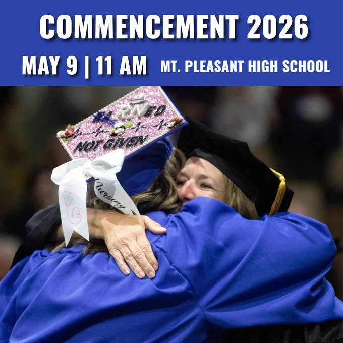 Graduate in blue gown with decorated cap hugging a faculty member during  commencement ceremony.