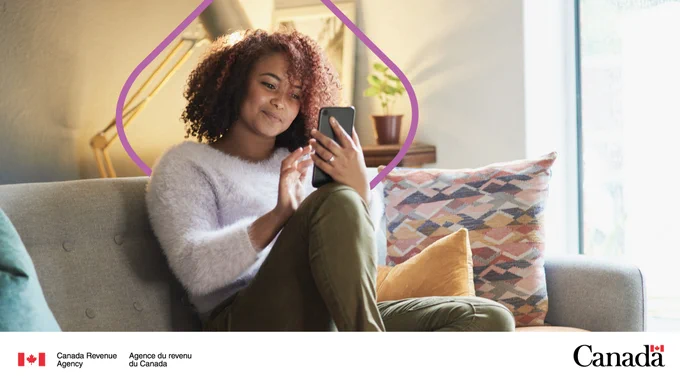 A person sits on a sofa. They are smiling while looking at their cellphone.