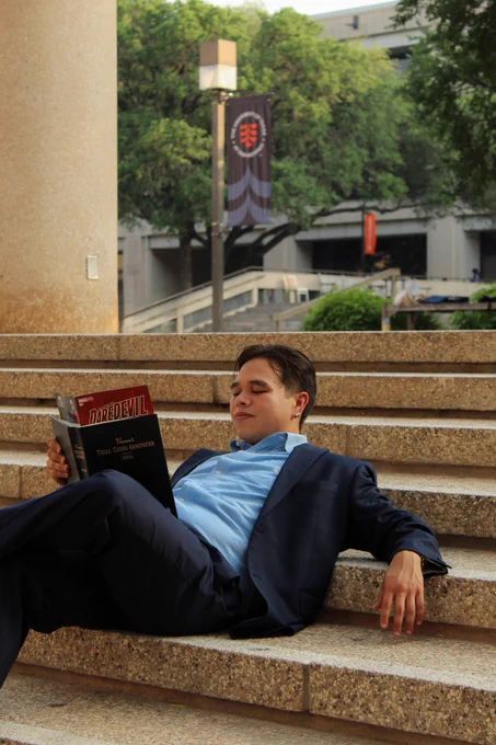 Jason Guevara reading two books simultaneously while sitting on a set of stairs on the UT San Antonio campus.