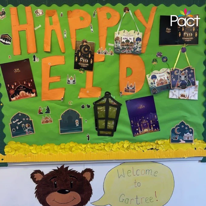 Decorated noticeboard with large “HAPPY EID” lettering, surrounded by cards, mosque illustrations and a lantern, with a “Welcome to Gartree” sign below.